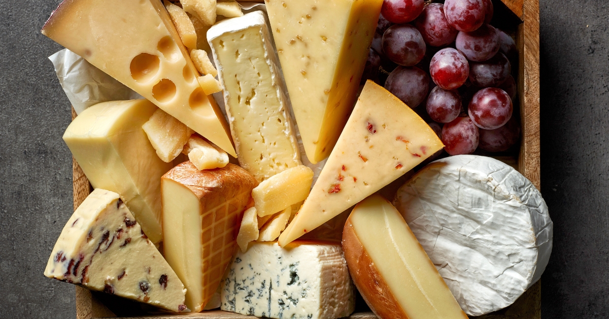 Various Types of Cheese with Fresh Grapes in a Wooden Board
