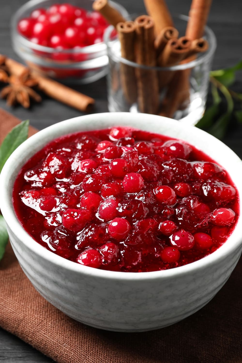 Bowl of cranberry sauces, dried cinnamon sticks and spices on the background