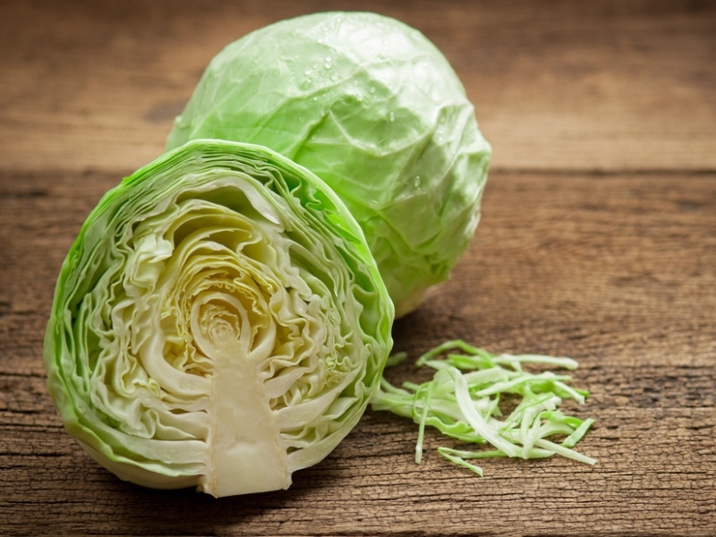Whole and sliced into half cabbage on a wooden table. 
