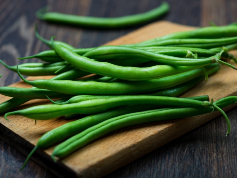 Fresh green beans on top of wooden cutting board. 