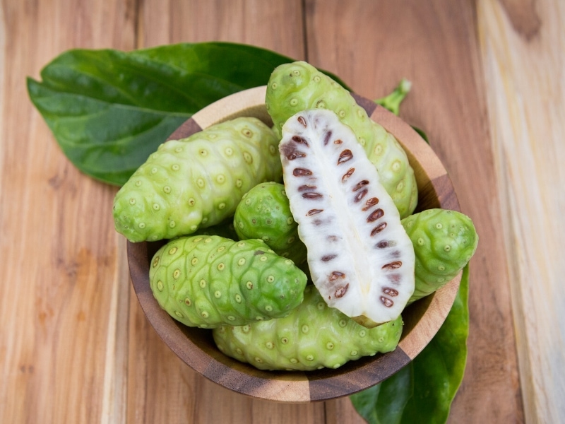 whole and sliced noni fruit in a bowl