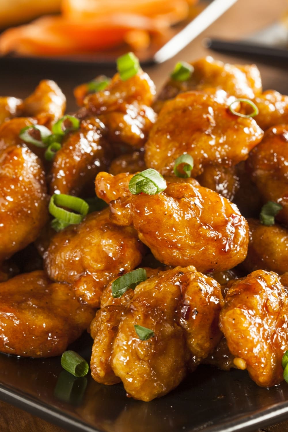 Closeup of Panda Express Orange Chicken Served on a Black Plate Topped With Chopped Onion Leaves