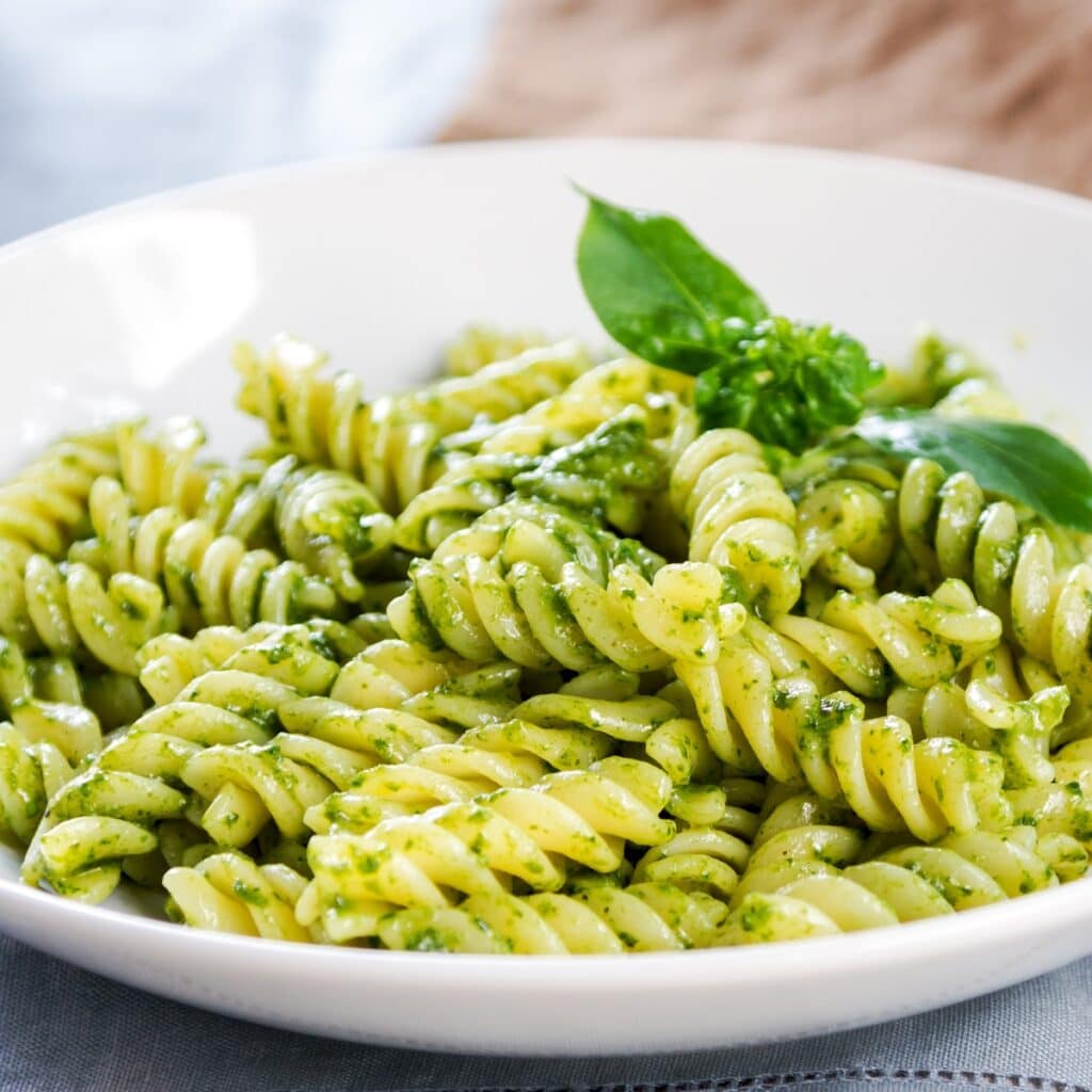 Pesto Pasta Garnished with Fresh Basil Leaves Served on a White Plate