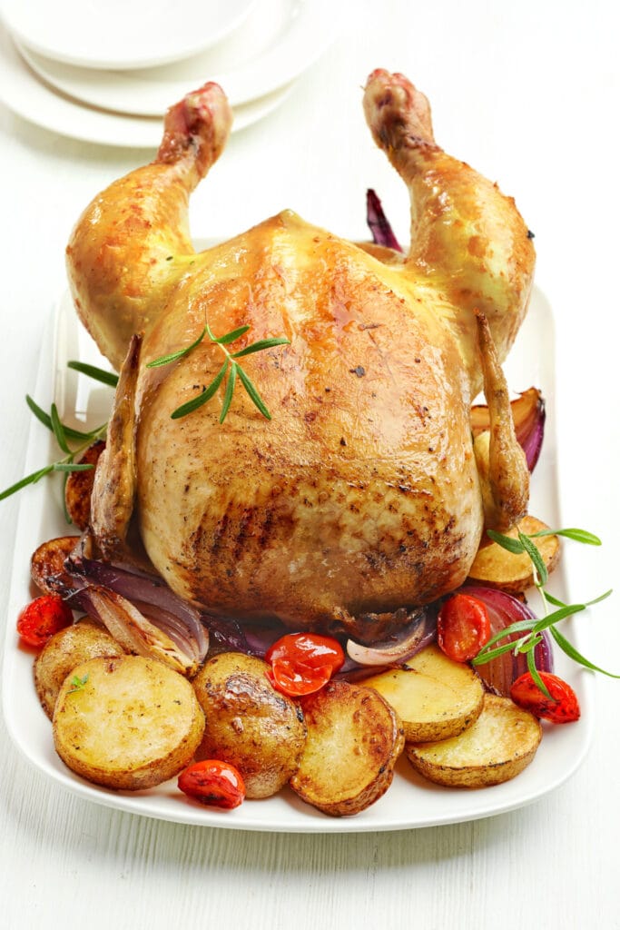 Roasted chicken with red onion, tomatoes, and potatoes on a white plate