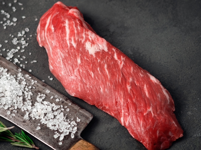 Raw Skirt Steak with Hatchet on a Stone Background