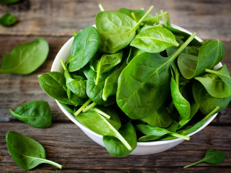 Bowl of fresh spinach leaves on a wooden table. 