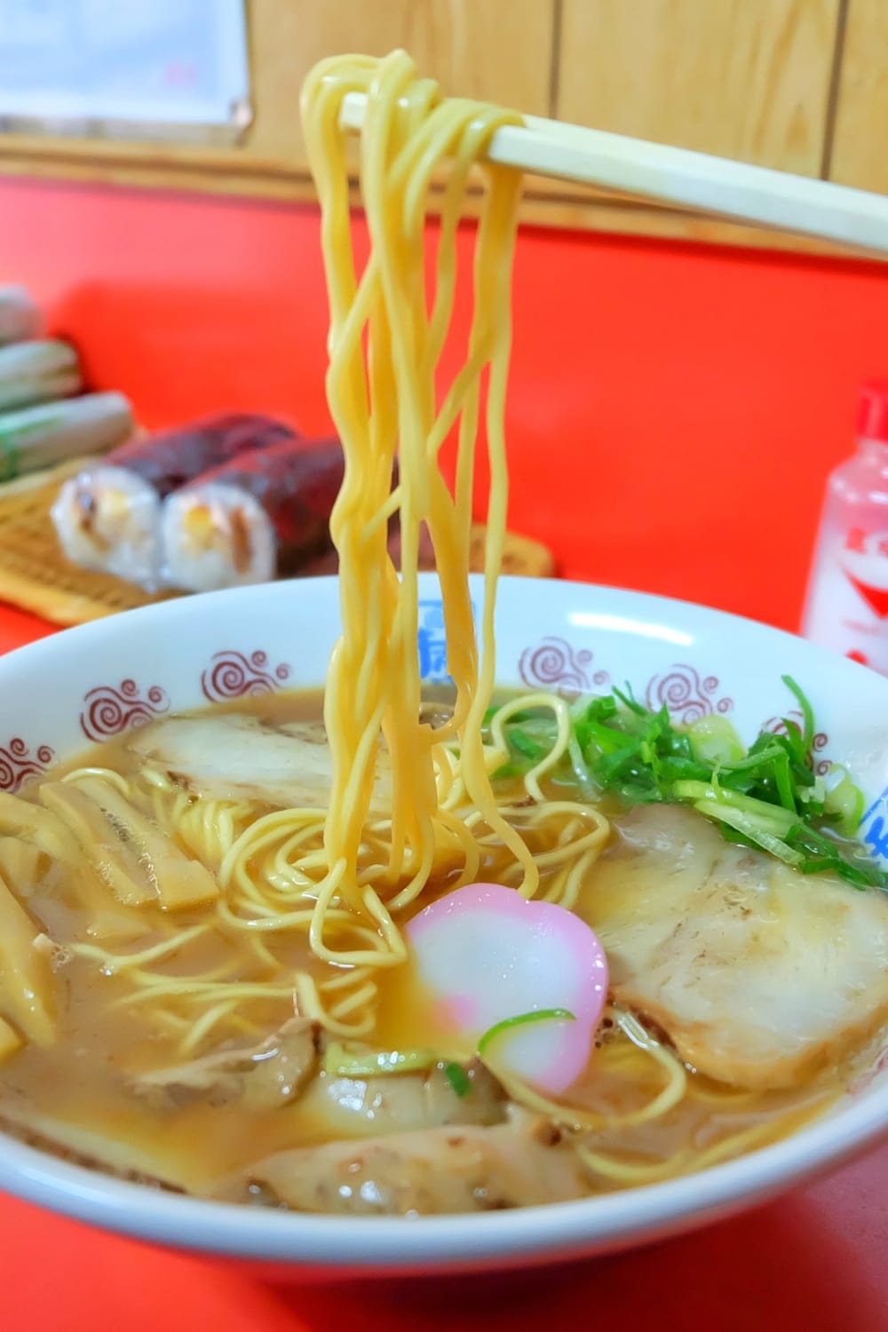 Wakayama Ramen served in a bowl made with egg noodles, ton katsu, bamboo shoots and mushroom place  on a red table.