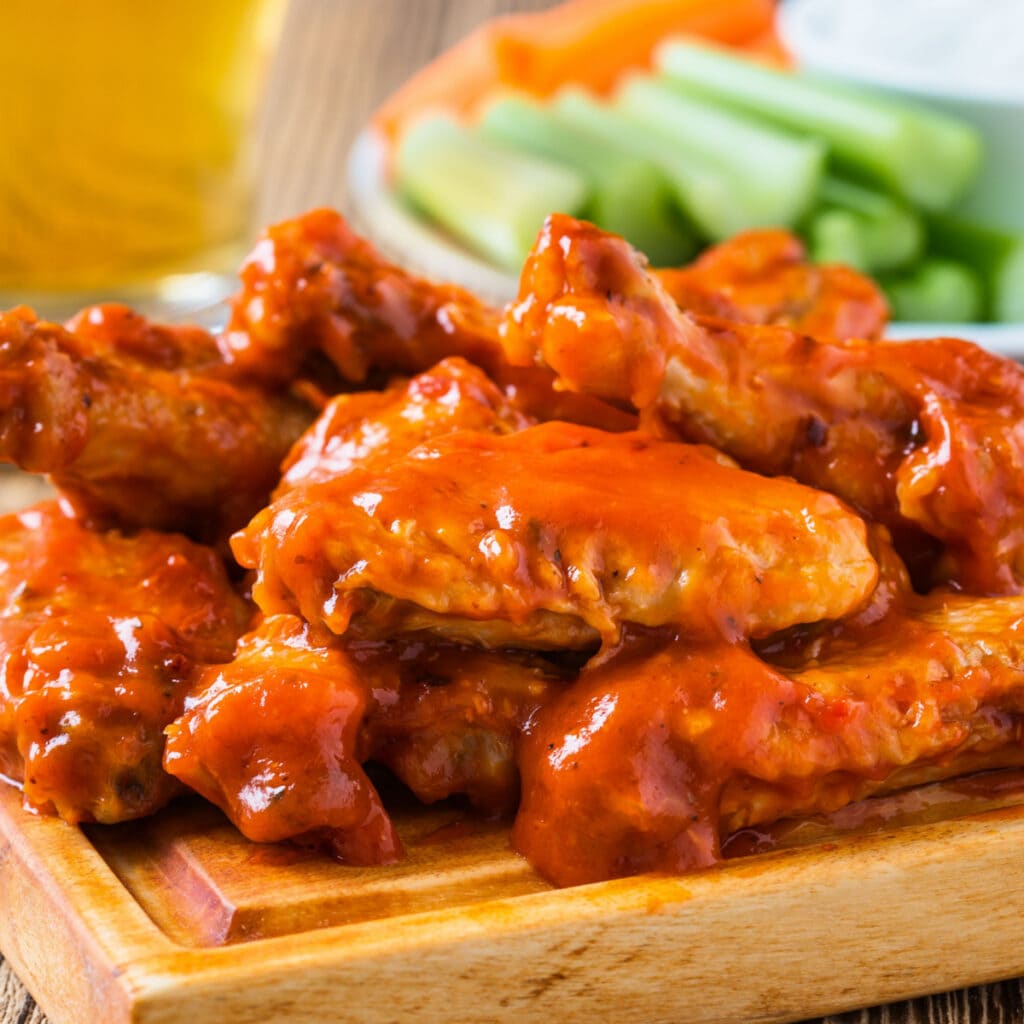 Pile of saucy buffalo chicken wings on a chopping board