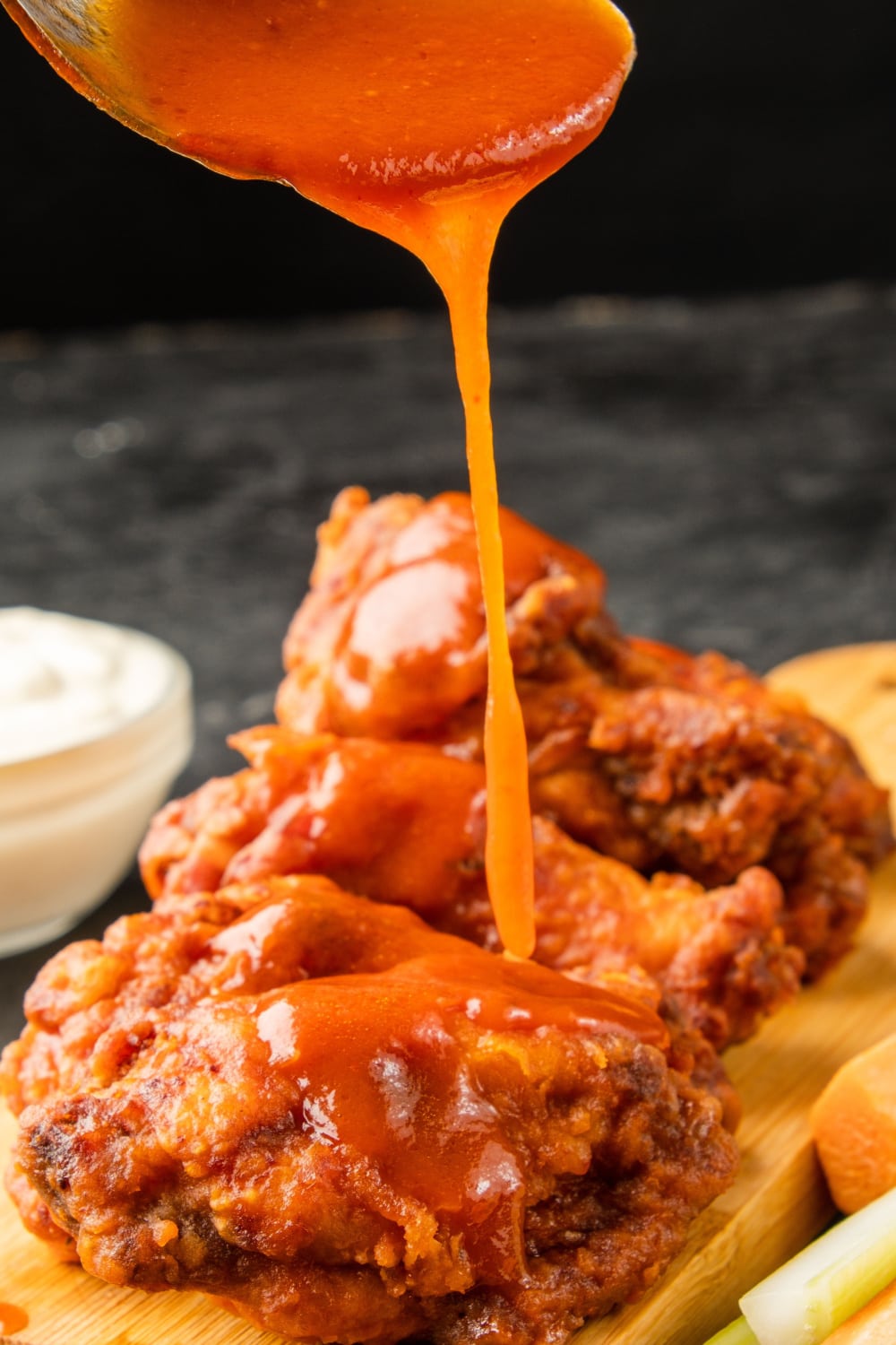 Buffalo Chicken Wing Sauce Drizzled over Fried Chicken Wings Placed on Top of a Wooden Board
