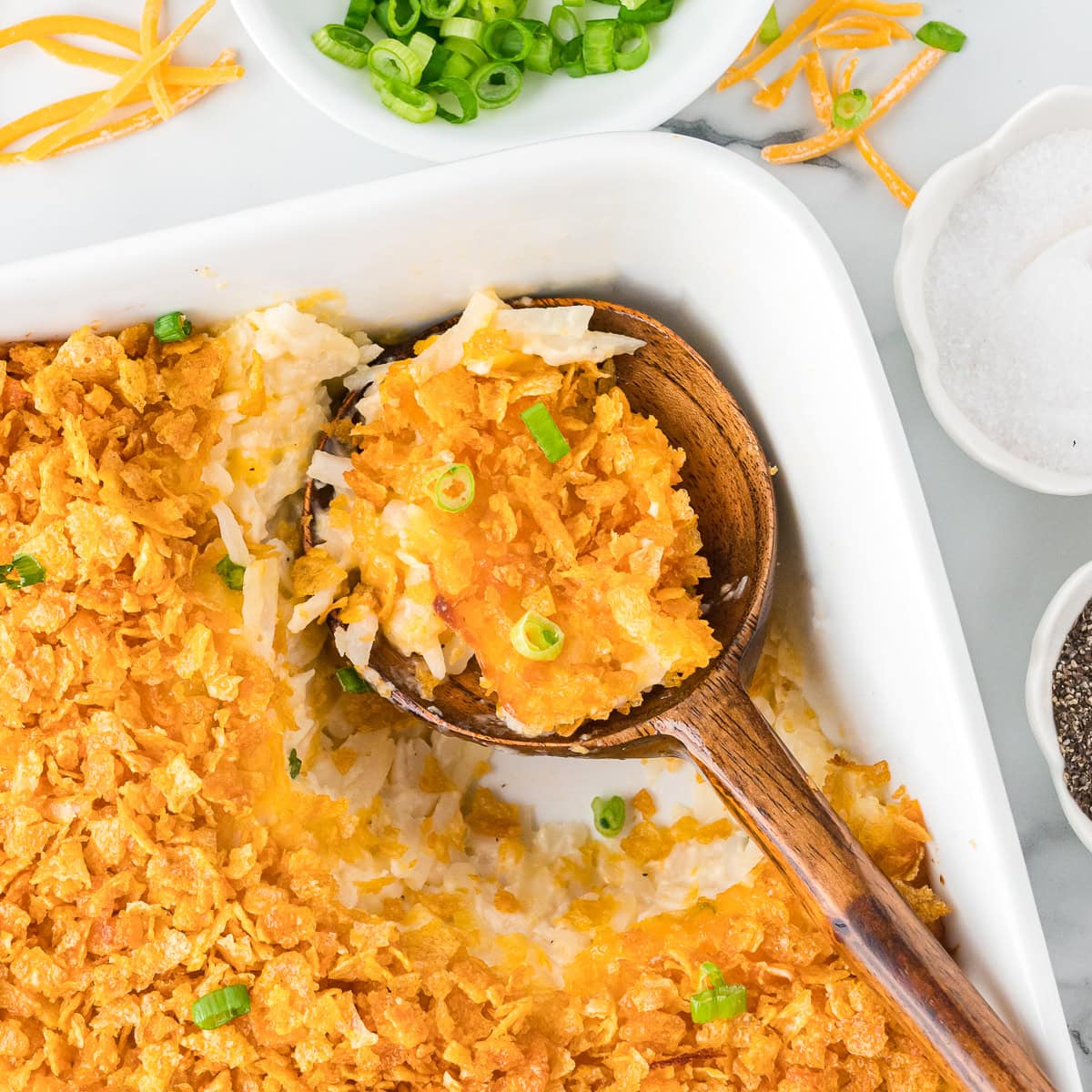 Cheesy potato casserole with green onions in a baking dish, featuring a wooden laddle