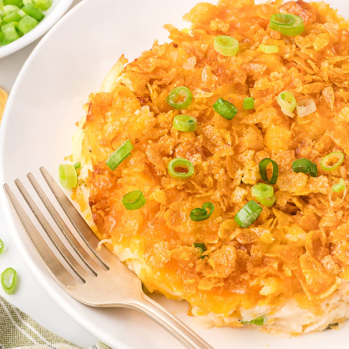 Cheesy potato casserole with green onions in a plate with fork on the side
