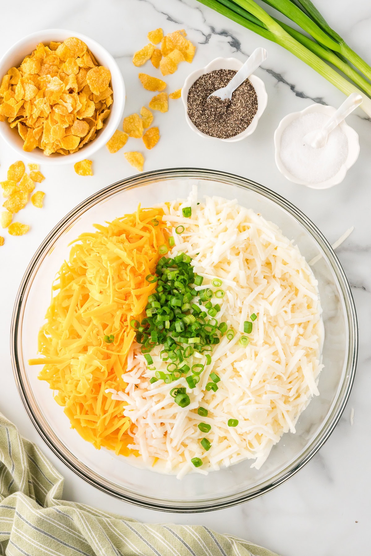 Cheese, hash browns potatoes and gree onions in a glass bowl