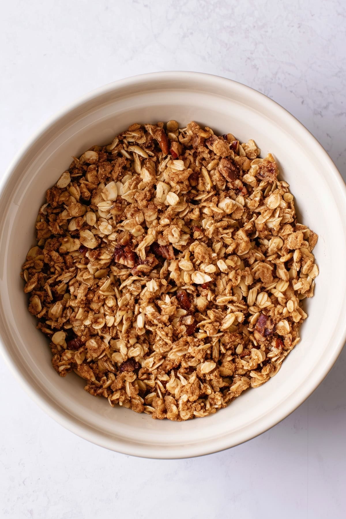 Rolled oats and chopped pecans in a white bowl, top view