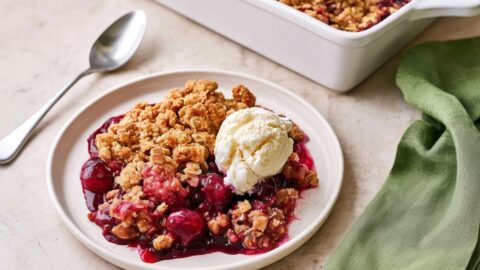 Cherry crisp in a white plate with a scoop of ice cream with kitchen towel on the side.