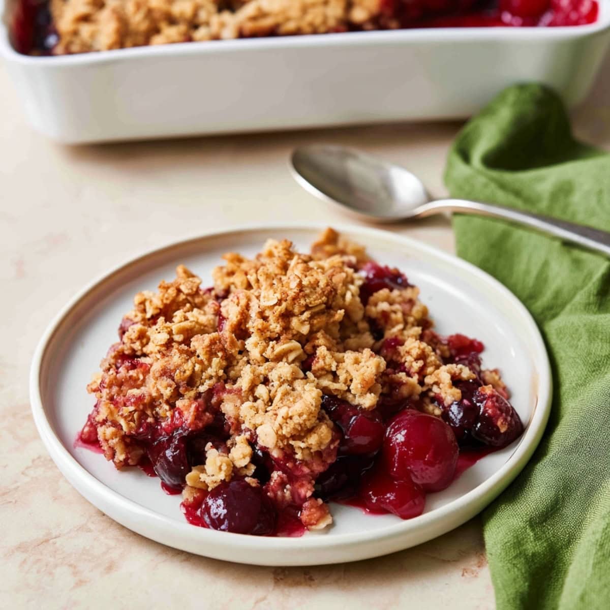 Cherry crisp with juicy cherries and crumb topping on a white plate.