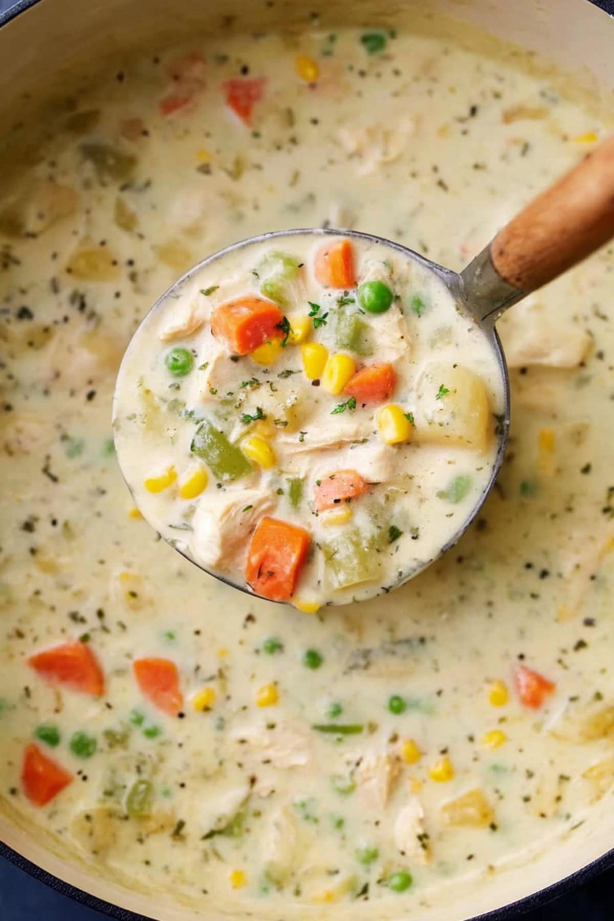 A laddle of chicken pot pie soup with carrots, corn, green peas and potatoes.