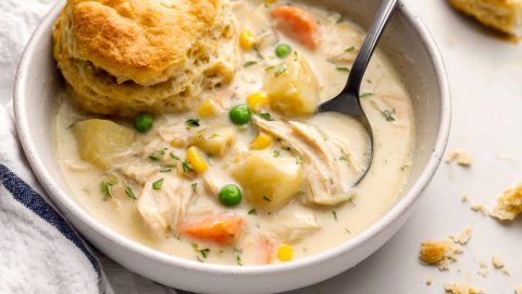 A bowl of chicken pot pie soup with mixed vegetable and a biscuit.