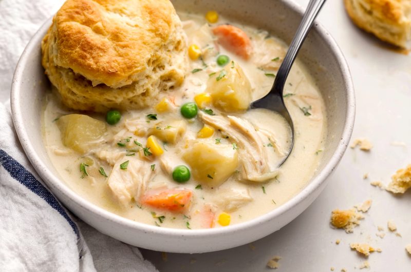 A bowl of chicken pot pie soup with mixed vegetable and a biscuit.