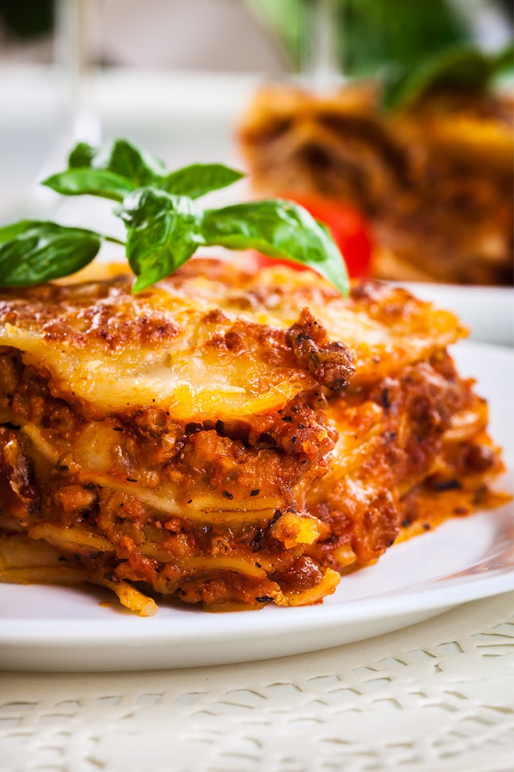 Slice of layers of lasagna, spaghetti sauce, cottage cheese and mozzarella cheese served on a plate with basil leaf on top