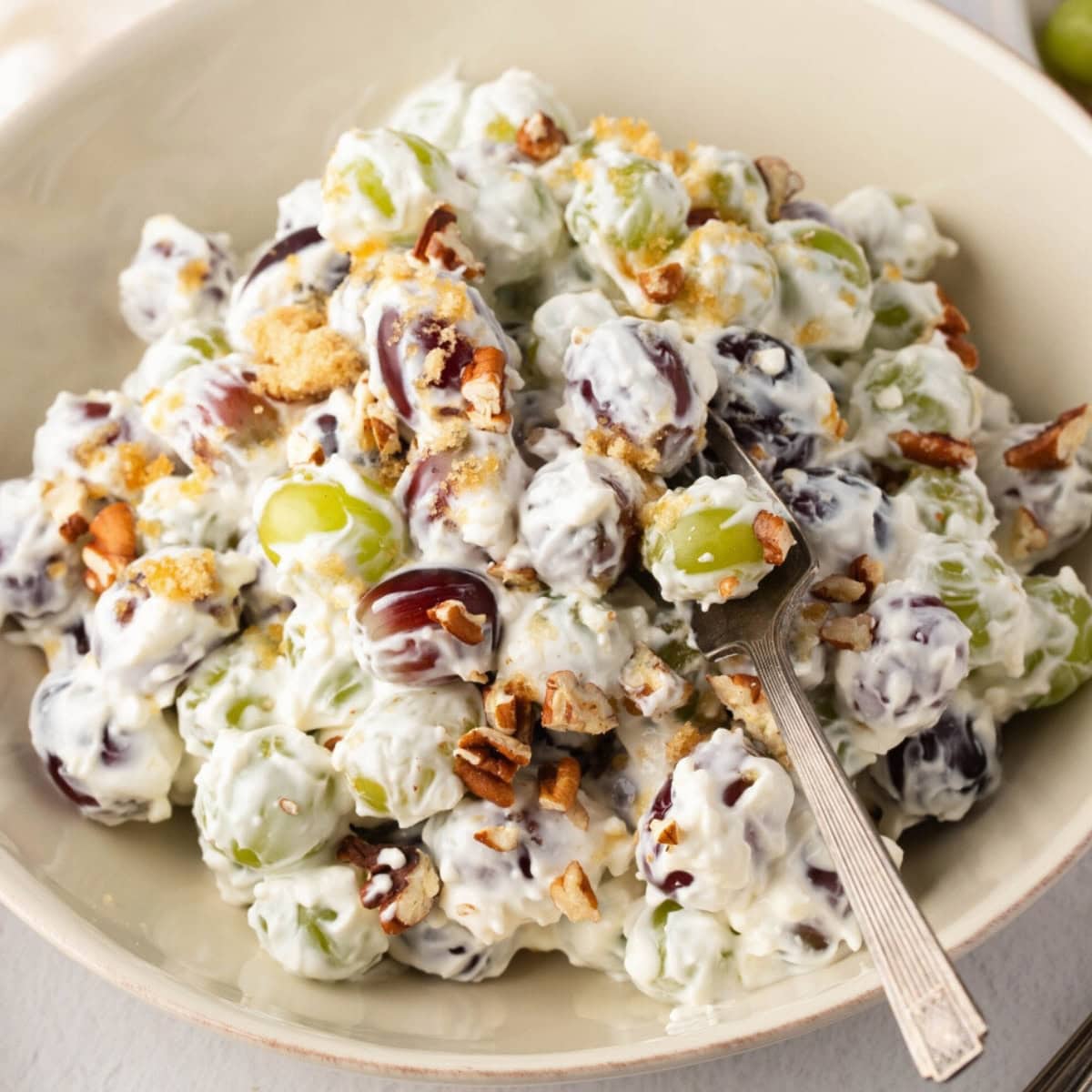 A bowl of creamy grape salad with pecans and brown sugar.
