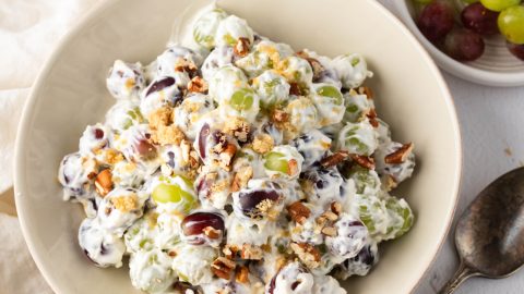 Creamy grape salad with cream cheese mixture, nuts and brown sugar in a bowl, spoon on the side.