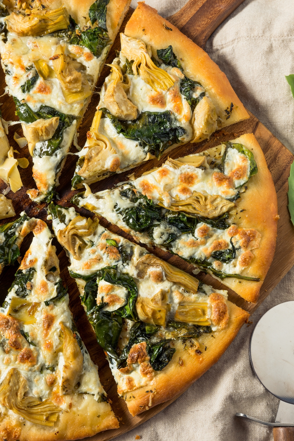 Sliced Homemade Artichoke and Spinach Pizza on a Wooden Serving Board