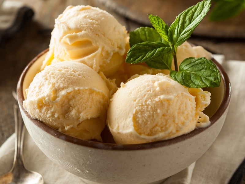 Four scoops of vanilla ice cream in a bowl with fresh mint