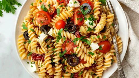 A serving plate of Ina Garten pasta salad with tomatoes, olives and feta, top view.