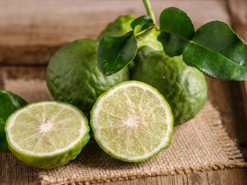 Kaffir Limes Whole and Sliced with Leaves on a Rustic Cloth