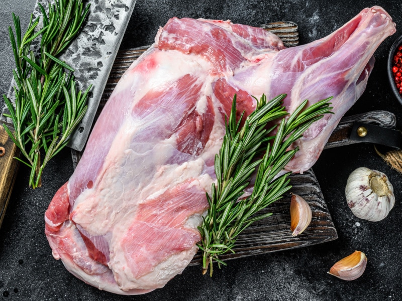 Raw Lamb Shoulder with Garlic and Rosemary on a Cutting Board