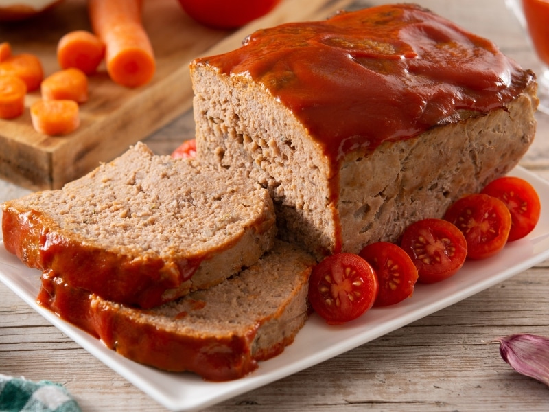 Meatloaf on a White Serving Plate with Tomatoes and Ketchup on Top