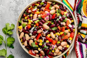 Top View of Mexican Bean Salad in a Bowl with a Colorful Mexican Cloth and Cilantro on the Side