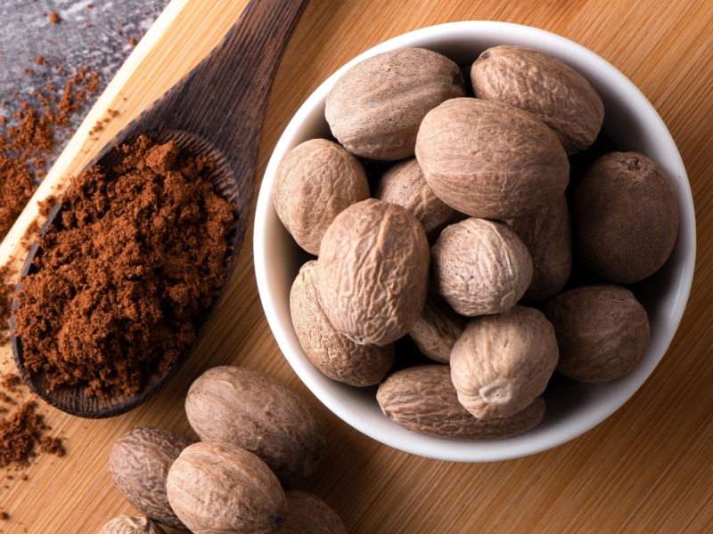Whole Nutmeg in a Bowl and Nutmeg Powder on a Wooden Spoon