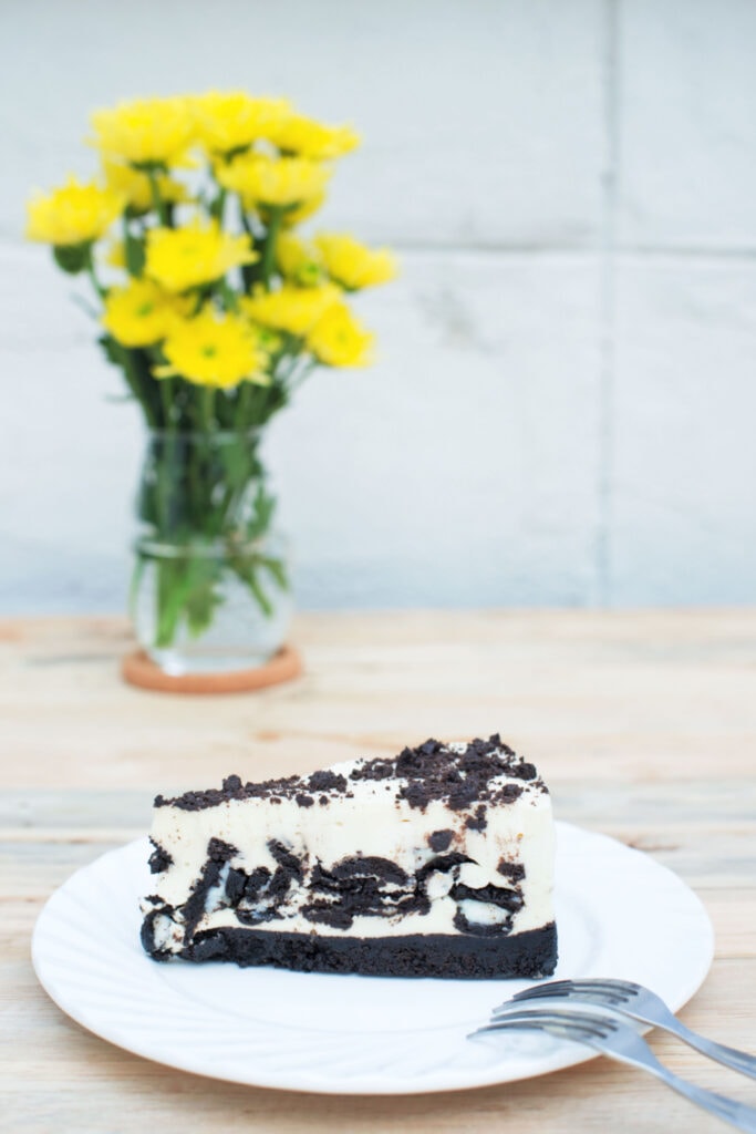 Philadelphia Oreo Cheesecake on white plate with flower vase on the background