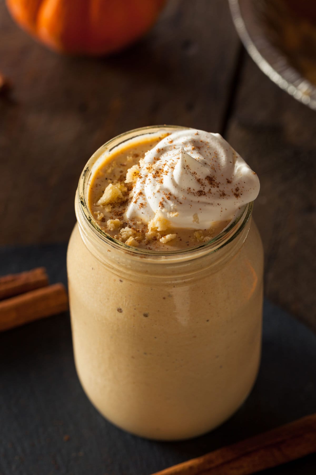 Glass of Pumpkin Pie Milkshake topped with whipped cream, sprinkled with cinnamon powder. 