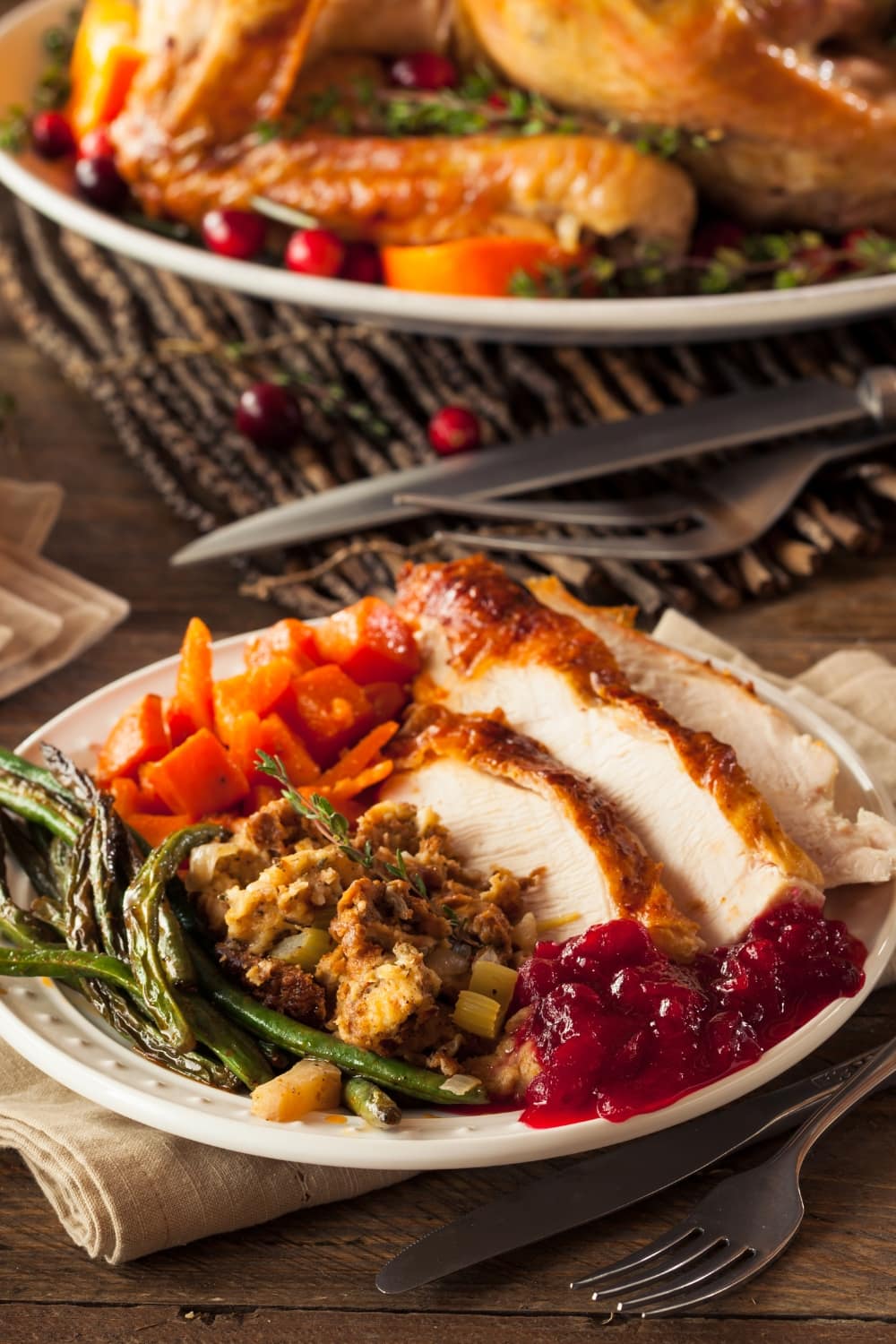 A serving of sliced roasted turkey, green beans, carrots and cranberry sauce.
