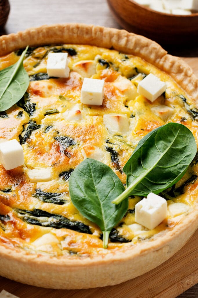 Spinach Quiche Garnished With Fresh Spinach Leaves and Diced Feta Cheese