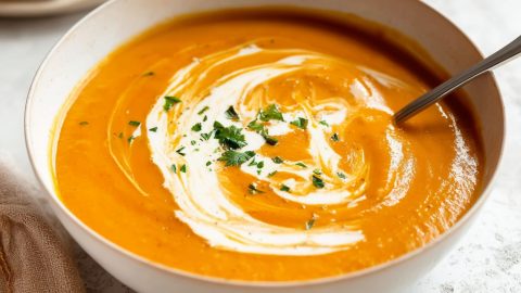 A close-up of sweet potato soup with yogurt and herbs in a white bowl.