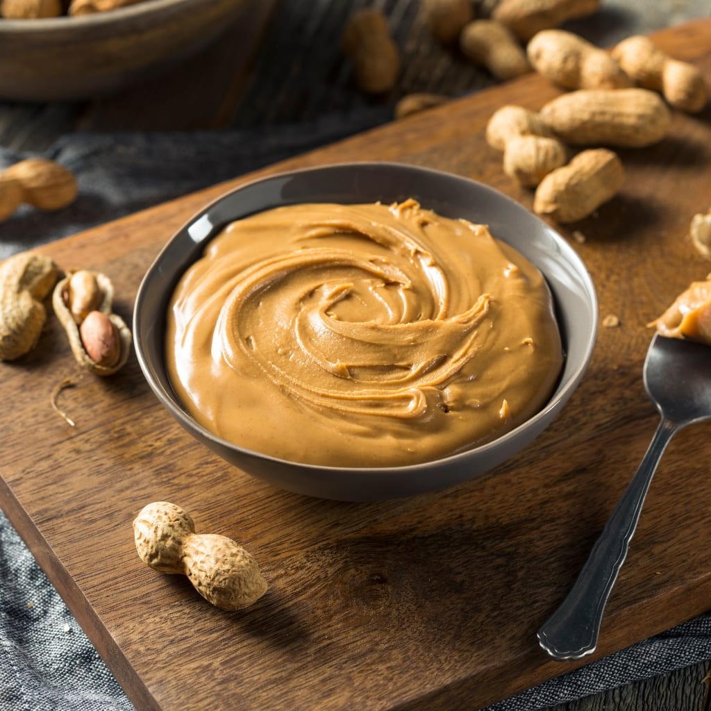 Bowl of sweet peanut butter on a table with peanuts and a spoon