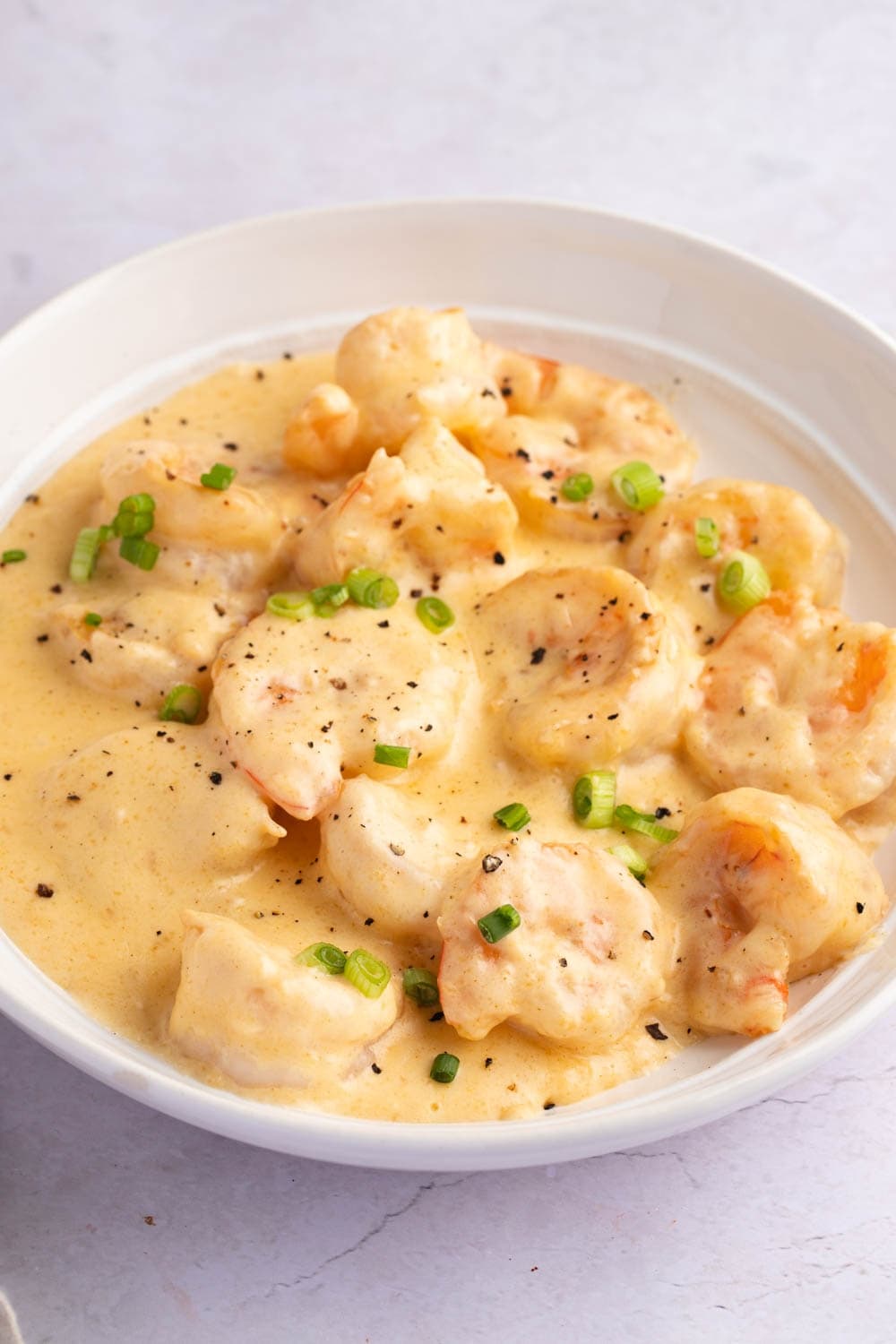 Creamy Shrimp Newburg in a White Bowl, Garnished With Sliced Onions and Black Pepper