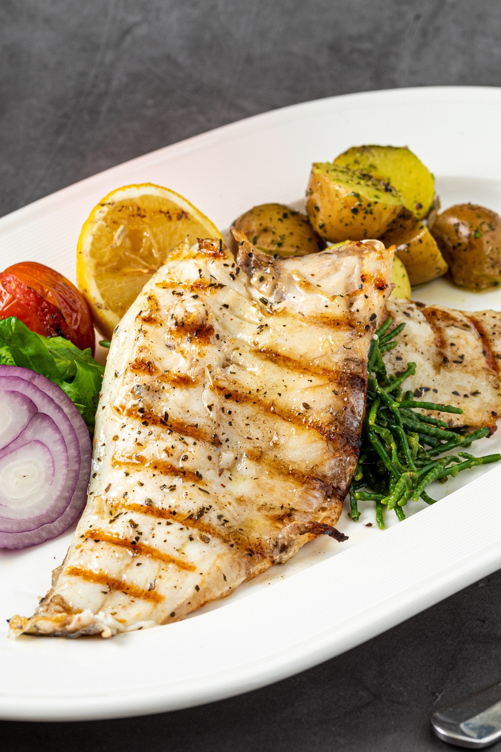 Grilled Sea Bass Fillet with Potatoes, Sliced lemon, Tomatoes, Red Onions and Greens