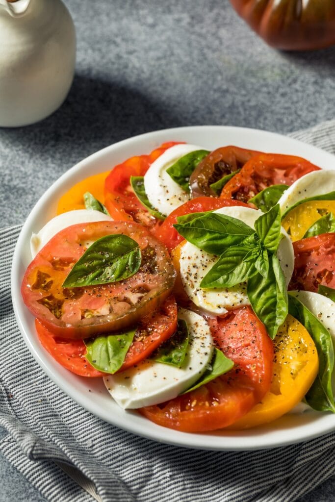 Healthy Heirloom Tomato Caprese Salad With Sliced Mozzarella Cheese and Fresh Basil Leaves, Seasoned With Pepper