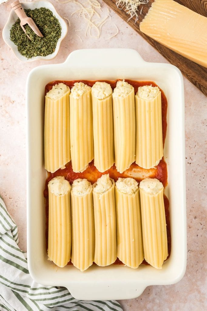 Manicotti pasta shells stuffed with ricotta cheese filling on a bed of marinara sauce in a white baking dish, top view.