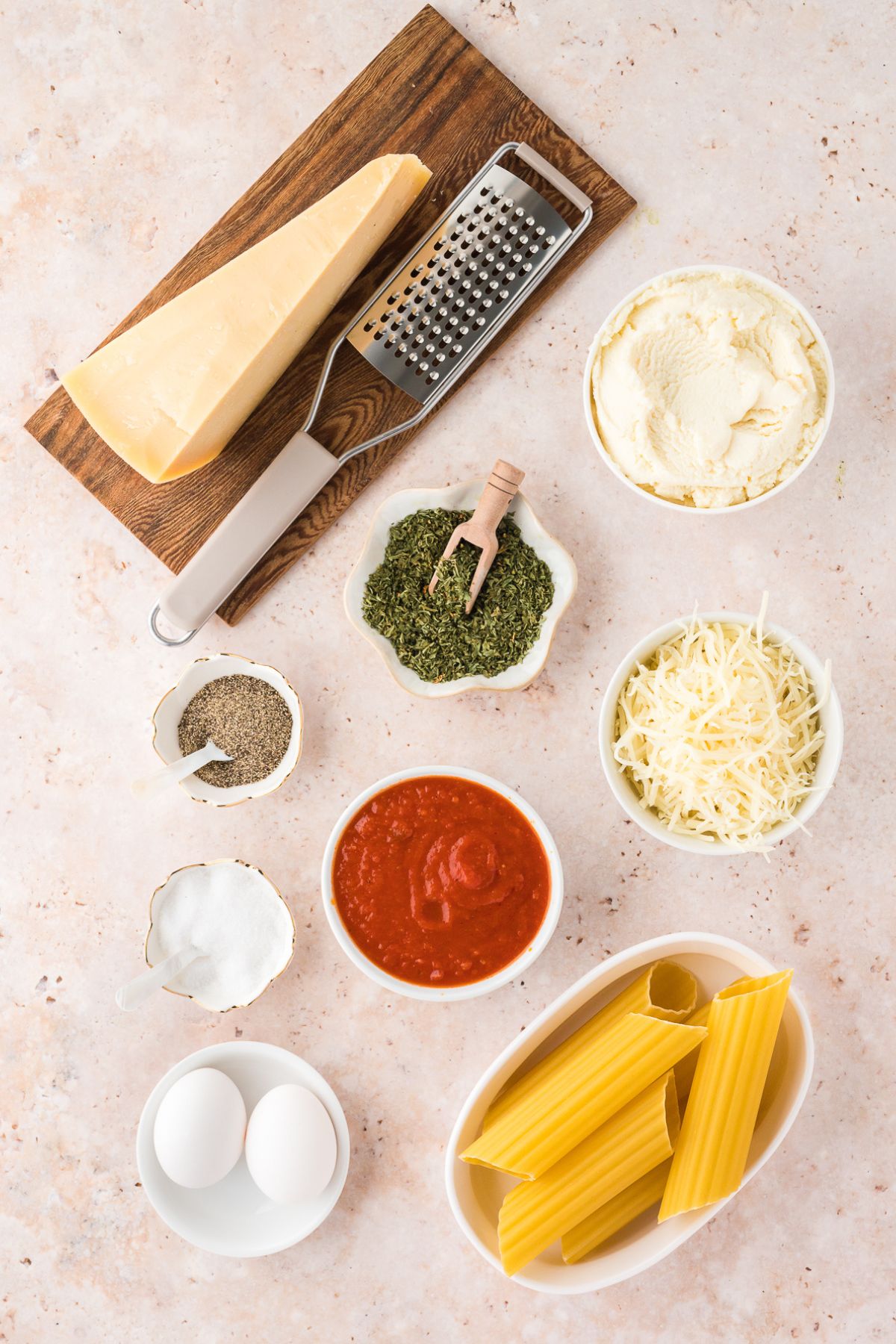 No-Boil Manicotti Ingredients: Manicotti pasta shells, ricotta cheese, mozzarella cheese, parmesan cheese, eggs, parsley, salt and pepper, and marinara sauce, top view.
