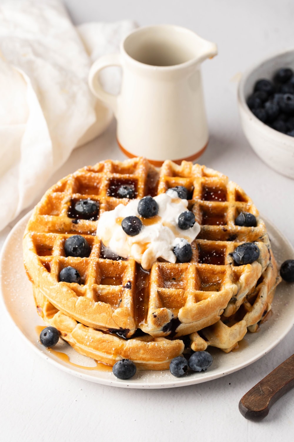 Stack of waffles with blueberries and whipped cream garnish served in a white plate.