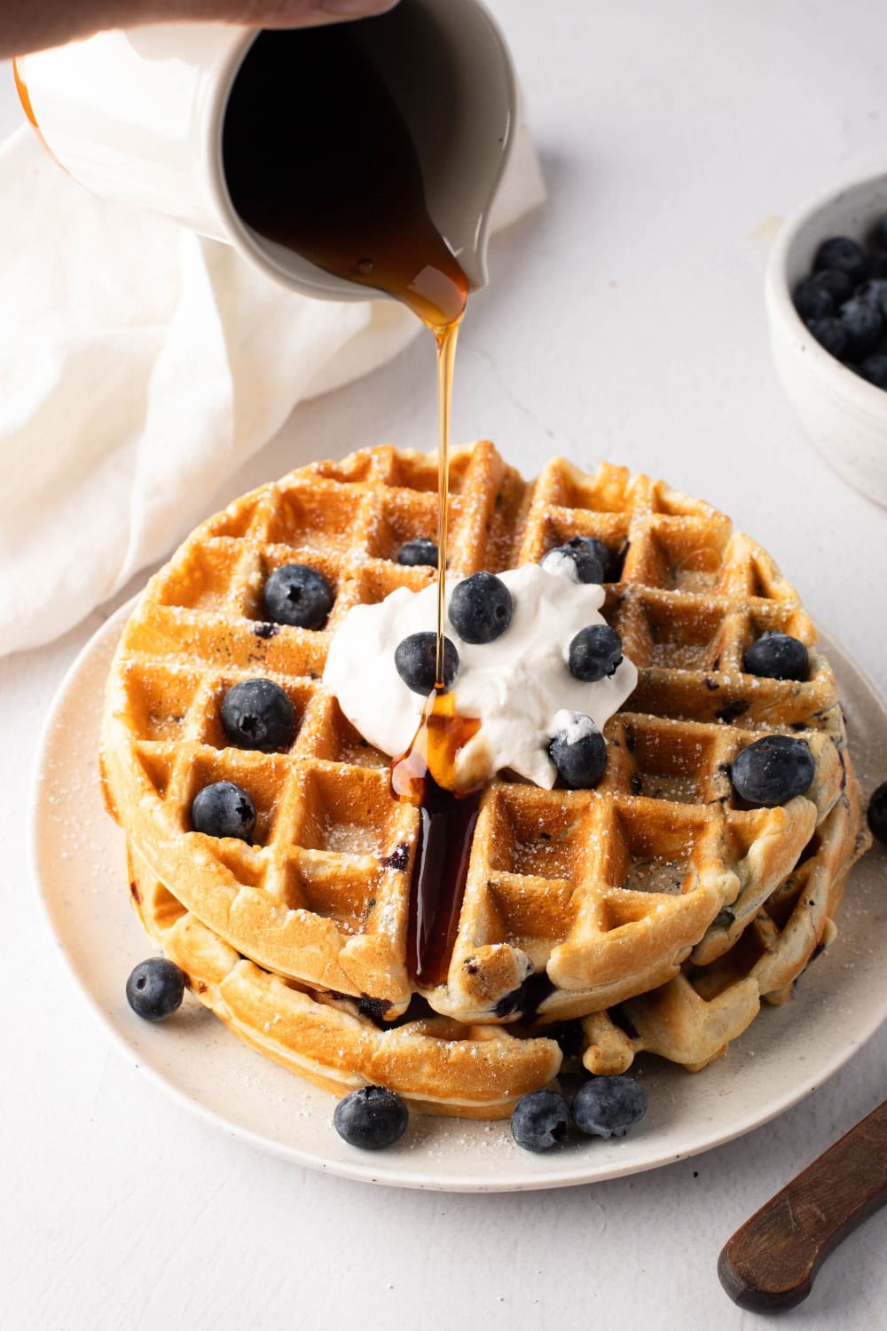 Maple syrup poured over blueberry waffle served in a white plate.