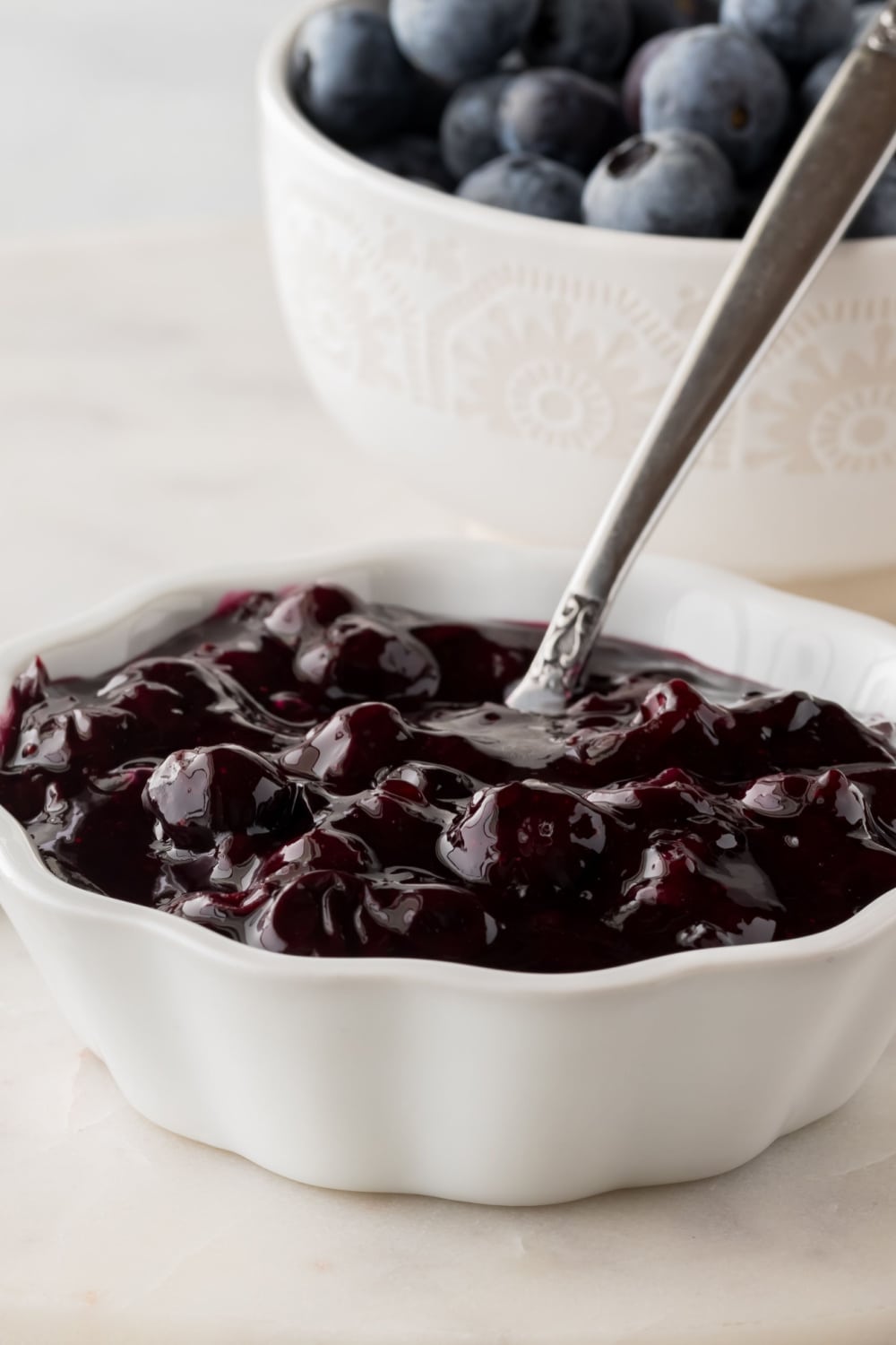 Spoon Dipped on a Bowl of Blueberry Sauce and a Bowl of Fresh Blueberries in the Background