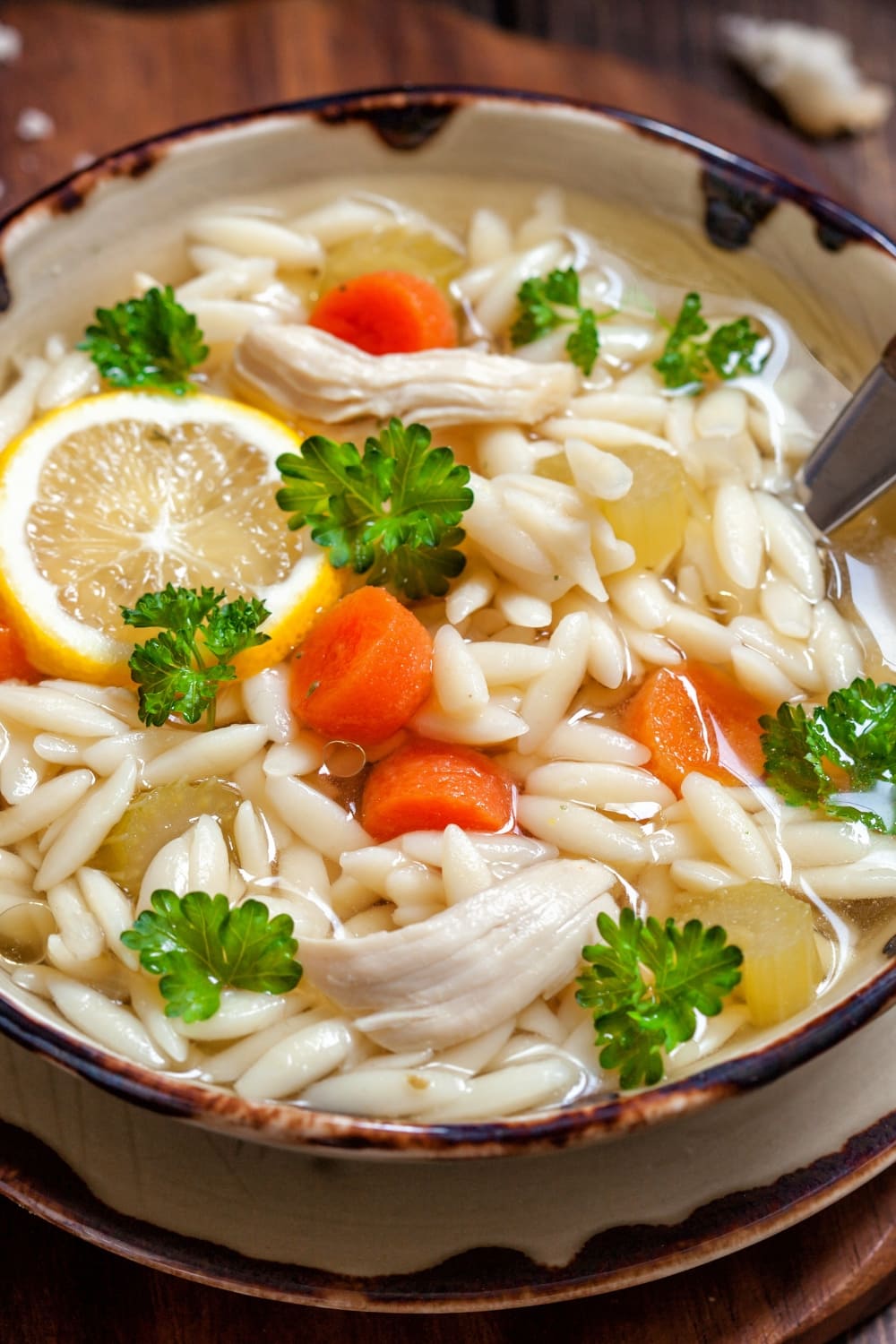 Bowl of Chicken Orzo Soup Made with Carrots, Chicken Meat and Orzo Pasta, Garnished With Fresh Parsley and Lemon Slice