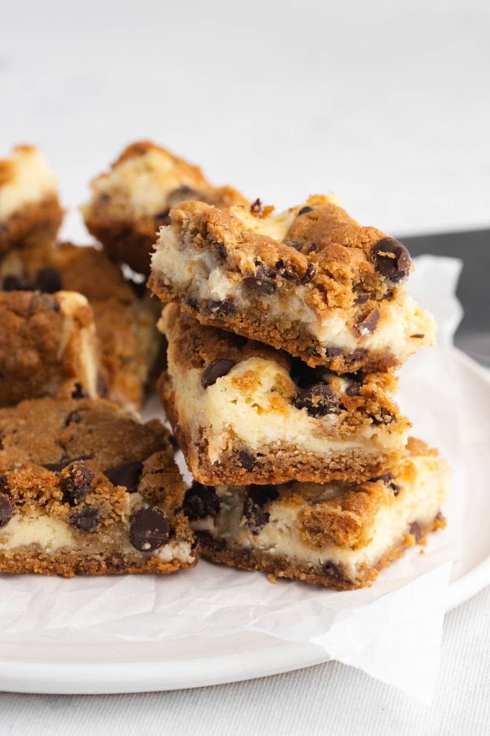 Chocolate Chip Cheesecake Bars Stacked on a White Plate With Parchment Paper