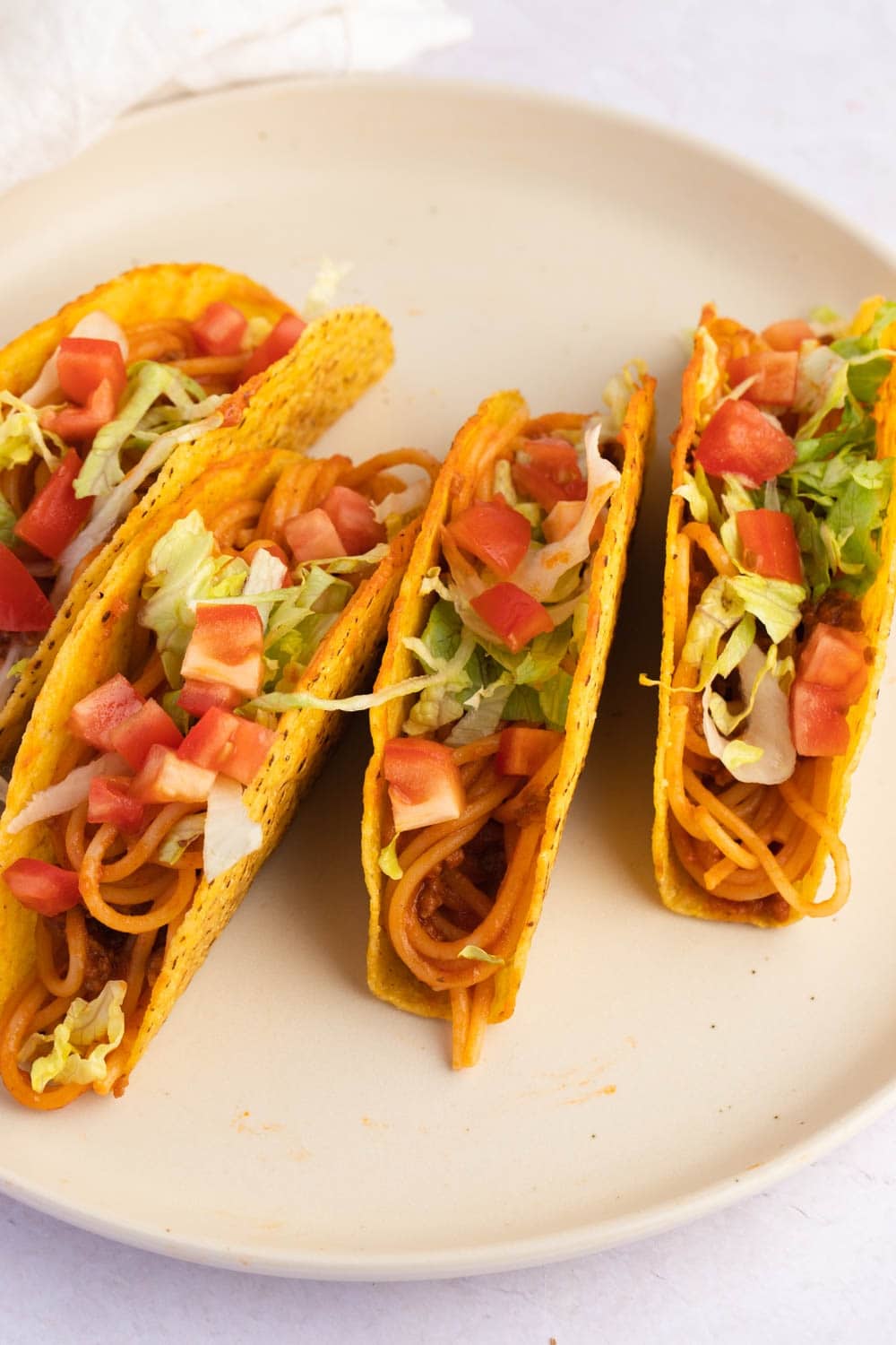 Spaghetti Tacos Made From Spaghetti Served on Taco Shells Garnished With Sliced Tomatoes, White Onions and Lettuce